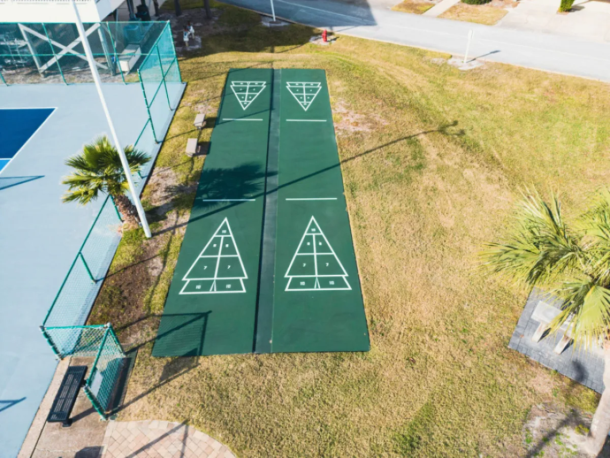 A cheerful outdoor recreation area featuring shuffleboard courts, palm trees, benches, and a tennis court, inviting families to enjoy friendly competitions and relaxation. The vibrant, communal atmosphere encourages outdoor play and social gatherings.
