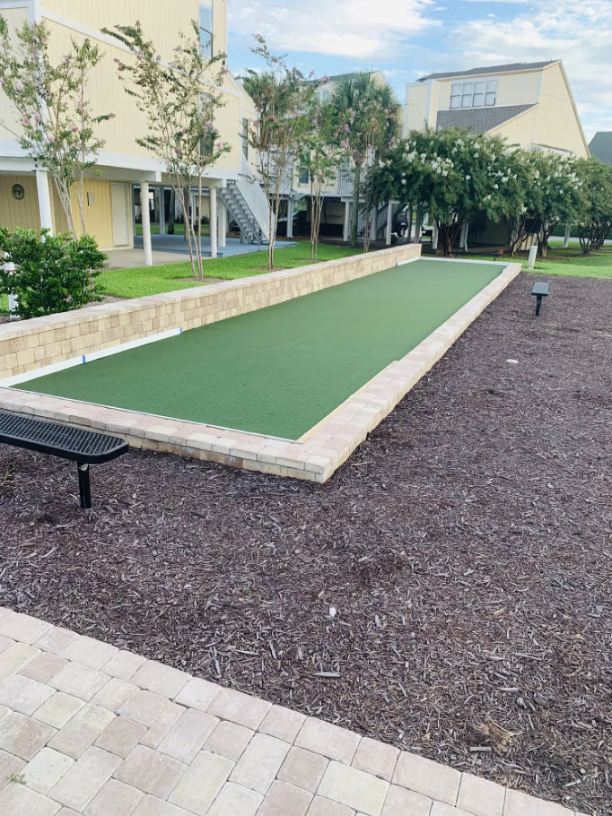 This image features a bocce ball court set amidst landscaped grounds, with benches for relaxation and mature trees providing shade. The inviting communal atmosphere hints at shared outdoor spaces for both recreation and casual walks with pets.