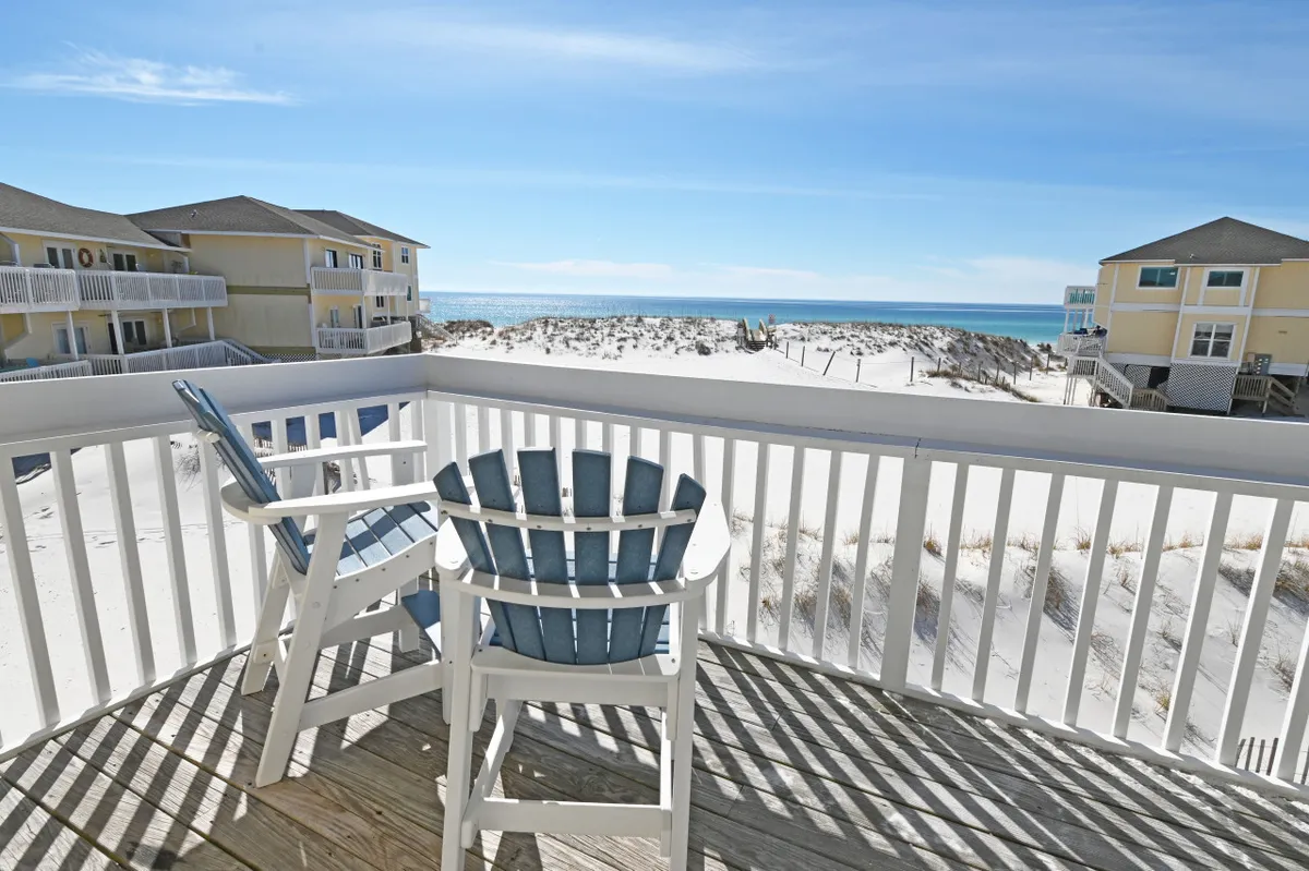 A stunning beachfront view with white sand and the turquoise blue ocean stretching to the horizon. Adirondack chairs are set up for relaxation, providing an inviting spot for morning coffee, reading, or watching the sunset. The scene evokes tranquility and luxury with a romantic, peaceful vibe.