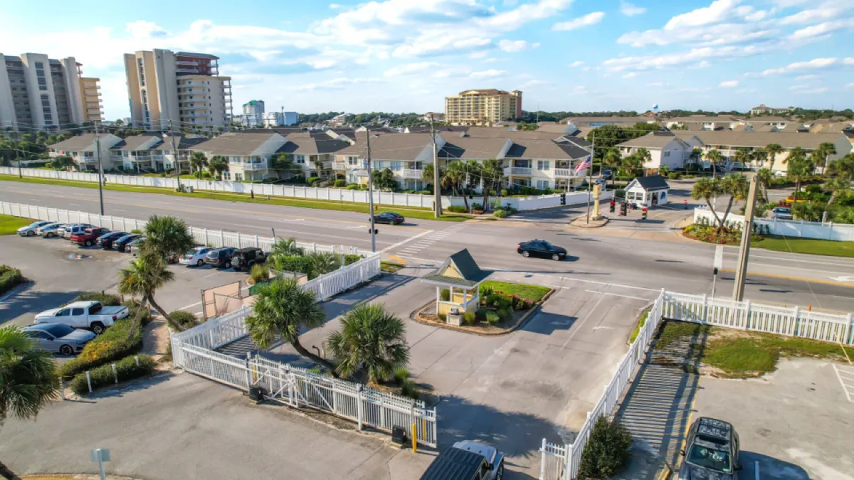 This image captures the gated entrance to the Sandpiper Cove community, complete with a guardhouse, white picket fencing, and a glimpse of residential buildings beyond. The secure, well-maintained entryway signals a safe and welcoming environment for all guests—including those with pets.